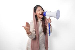energiek Aziatisch moslim vrouw vervelend sluier hijab geschreeuw Bij megafoon terwijl verhogen hand- net zo uitnodigend of laten we Gaan gebaar. Ramadan en eid mubarak concept foto