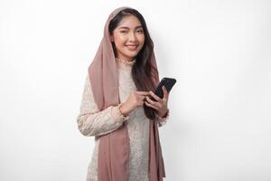 vrolijk jong Aziatisch moslim vrouw in sluier hijab glimlachen en gevoel gelukkig terwijl Holding een smartphone. Ramadan en eid mubarak concept foto