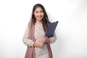 portret van Aziatisch moslim vrouw in hoofddoek sluier hijab staand en glimlachen gelukkig terwijl Holding een document kaart. Ramadan concept foto