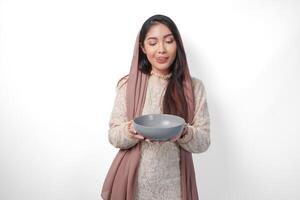 portret van een hongerig Aziatisch moslim vrouw Holding kom denken wat naar eten na vastend met kopiëren ruimte over- de schaal, geïsoleerd wit achtergrond foto