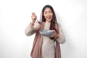 gelukkig Aziatisch moslim vrouw Holding kom en bestek naar eten na vastend terwijl glimlachen vrolijk Aan geïsoleerd wit achtergrond. Ramadan concept foto