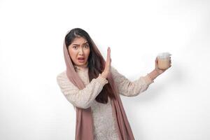 een echt jong Aziatisch moslim vrouw vervelend sluier hijab gebaren afwijzing naar een kop van koffie Aan vastend maand, geïsoleerd door wit achtergrond. Ramadan concept foto