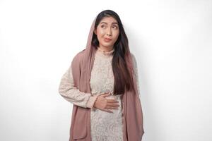 portret van Aziatisch moslim vrouw vervelend hoofddoek sluier plaatsen handen Aan de maag gevoel hongerig en willen naar eten terwijl vasten, geïsoleerd over- wit achtergrond. Ramadan en eid mubarak concept foto