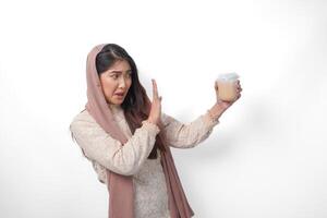 een echt jong Aziatisch moslim vrouw vervelend sluier hijab gebaren afwijzing naar een kop van koffie Aan vastend maand, geïsoleerd door wit achtergrond. Ramadan concept foto