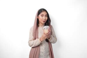 portret van Aziatisch moslim vrouw in hoofddoek sluier hijab gevoel dorstig na vastend en drinken koffie in een plastic beker. Ramadan concept foto