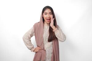 jong Aziatisch vrouw vervelend hoofddoek sluier hijab is verhogen handen en geschreeuw met mond breed open, geïsoleerd wit achtergrond foto