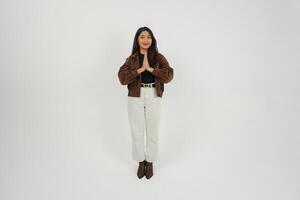 een vol lichaam portret van Aziatisch jong vrouw met gewoontjes kleding maken groet gebaar met twee handen terwijl lachend, staand Aan geïsoleerd wit achtergrond foto