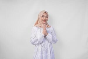 mooi Aziatisch moslim vrouw vervelend wit jurk en hijab glimlachen terwijl aan het doen formeel Welkom of groet gebaar, staand over- geïsoleerd wit achtergrond foto