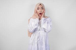 portret van jong Aziatisch moslim vrouw vervelend wit jurk en hijab met verrast uitdrukking en mond breed Open na horen schokkend nieuws over- geïsoleerd wit achtergrond foto