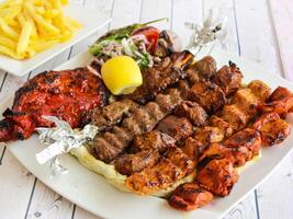 mengen rooster schotel met kip tikka, rundvlees kabab, schapenvlees kebab, seekh kabab en lam karbonade met salade en Patat geserveerd in schotel geïsoleerd houten tafel top visie van tandoori rooster bbq voedsel foto