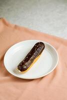 chocola eclair geserveerd in bord geïsoleerd Aan servet kant visie van cafe gebakken voedsel Aan achtergrond foto