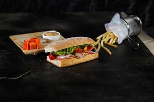 ciabatta gerookt ham belegd broodje geïsoleerd Aan houten met mayonaise dip en Frans Patat emmer bord kant visie van Italiaans snel voedsel Aan grijs achtergrond foto