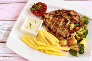 kip steak met Frans Patat, mayo duik, tomaat, broccoli en komkommer salade geserveerd in schotel geïsoleerd Aan tafel detailopname top visie van Fast food specerijen voedsel foto