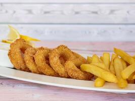 diep gebakken calamares inktvis ringen met Frans Patat geserveerd in schotel geïsoleerd Aan tafel detailopname top visie van gegrild zeevruchten foto