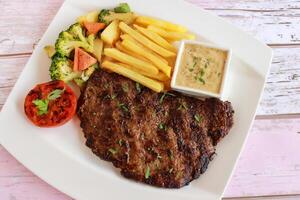 rundvlees steak met Frans Patat, mayo duik, tomaat, broccoli en komkommer salade geserveerd in schotel geïsoleerd Aan tafel detailopname top visie van Fast food specerijen voedsel foto