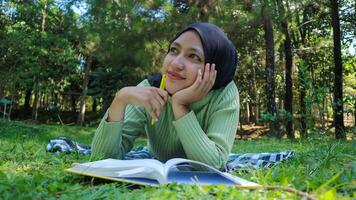 glimlachen moslim vrouw in hijab in park Holding boek en pen denken idee.leeg ruimte foto