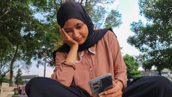 portret van glimlachen moslim vrouw in hijab in de stad park houden telefoon mobiel terwijl gestut haar kin foto