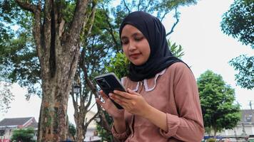 portret van moslim vrouw gebruik makend van mobiel telefoon lezing bericht Bij stad park. genieten van, ontspannende weekend foto