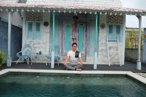 villa welzijn, Aziatisch Mens model- beoefenen yoga, lotus houding door zwembad, Bali Indonesië foto