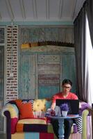 Aziatisch Mens werken Aan laptop in zonovergoten villa, sofa comfort, produktiviteit foto