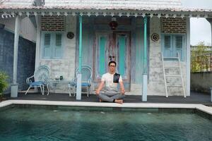 villa welzijn, Aziatisch Mens model- beoefenen yoga, lotus houding door zwembad, Bali Indonesië foto