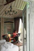 werk van huis, binnen- productiviteit, Aziatisch Mens Aan bank, werken Aan laptop, met villa zonnestraal foto