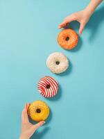 twee handen bereiken voor donuts Aan blauw achtergrond, top visie. creatief lay-out met heerlijk geglazuurd donuts. verticaal vlak leggen met diagonaal gemaakt van donuts of donuts foto