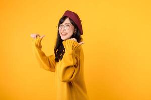 jong Aziatisch vrouw in haar jaren '30, vervelend een geel overhemd en rood baret. gelukkig gezicht en richten vinger naar vrij kopiëren ruimte tegen levendig geel achtergrond. ontgrendelen spaargeld en winkel nu foto