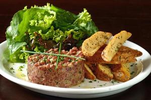 steak tartaar met blad salade en rustiek aardappelen foto