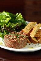 steak tartaar met blad salade en rustiek aardappelen foto