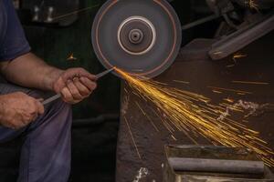 industrieel arbeider met hoek Slijper snijdend metaal met veel scherp vonken Aan werkplaats foto