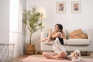 jong vrouw in sportkleding aan het doen meditatie praktijk en yoga met schattig hond in leven kamer, gezond levensstijl, mentaal Gezondheid concept. foto