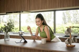 jong Aziatisch vrouw werken met tablet in de keuken Bij huis foto