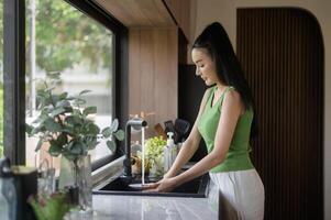 Aziatisch vrouw het wassen gerechten in de keuken wastafel Bij huis foto