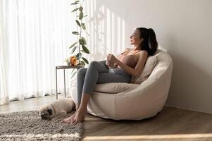 jong Aziatisch vrouw in sportkleding drinken zuiver water van glas in leven kamer Bij huis foto