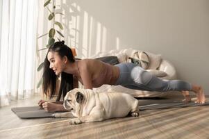 Aziatisch vrouw in sportkleding oefenen en aan het doen yoga met schattig hond in leven kamer Bij huis, gezond levensstijl, mentaal Gezondheid concept. foto