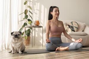 Aziatisch vrouw in sportkleding oefenen en aan het doen yoga met schattig hond in leven kamer Bij huis, gezond levensstijl, mentaal Gezondheid concept. foto