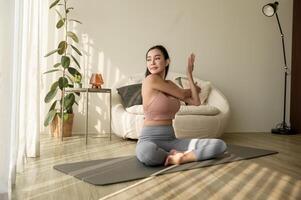 Aziatisch vrouw in sportkleding oefenen en aan het doen yoga in leven kamer Bij huis, gezond levensstijl, mentaal Gezondheid concept. foto