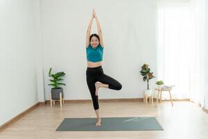 slank Aziatisch vrouw praktijk yoga werkzaamheid in flat of huis. Aziatisch vrouw aan het doen opdrachten in ochtend. evenwicht, meditatie, ontspanning, mooi zo Gezondheid, Vrolijk, kom tot rust, gezond levensstijl, eetpatroon, slank foto