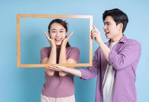 jong Aziatisch paar Holding foto kader Aan blauw achtergrond