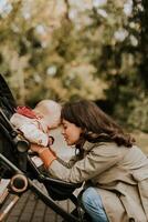 jong vrouw met schattig baby meisje in baby wandelwagen Bij de herfst park foto