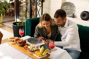 jong paar hebben lunch en drinken vers geperst sap terwijl op zoek Bij de mobiel telefoon in de restaurant foto