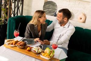 jong koppelgebruik mobiel telefoon terwijl hebben lunch en drinken vers geperst sap in de restaurant foto