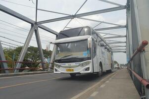 een groot damri bus was voorbijgaan Aan een ijzer truss brug, Indonesië, 16 januari 2024. foto