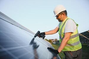 portret van glimlachen zelfverzekerd ingenieur technicus met elektrisch schroevendraaier, staand in voorkant van onvoltooid hoog buitenkant zonne- paneel foto voltaïsch systeem