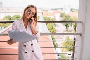 bedrijf vrouw Aan de telefoon Bij kantoor. jong bedrijf vrouw hebben telefoon telefoontje Bij de kantoor. glimlachen bedrijf vrouw. mooi jong bedrijf gebruik makend van smartphone Bij de zolder kantoor. foto