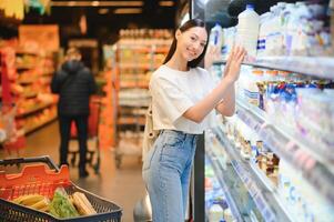 jong glimlachen gelukkig vrouw Jaren 20 in gewoontjes kleren boodschappen doen Bij supermarkt op te slaan met kruidenier kar foto