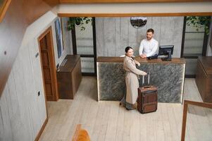 elegant bedrijf vrouw met reizen trolley bagage in hotel lobby foto