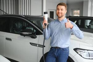 een gelukkig Mens kiest een nieuw elektrisch auto Bij een auto dealerschap. de concept van buying een ecologisch auto foto