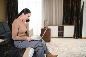 zakenvrouw met laptop computer zittend in hotel Aan bed en werken laat in hotel kamer, met haar laptop computer foto